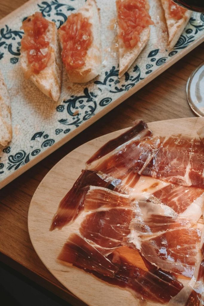 Jamón ibérico en tabla junto a tostadas con tomate.